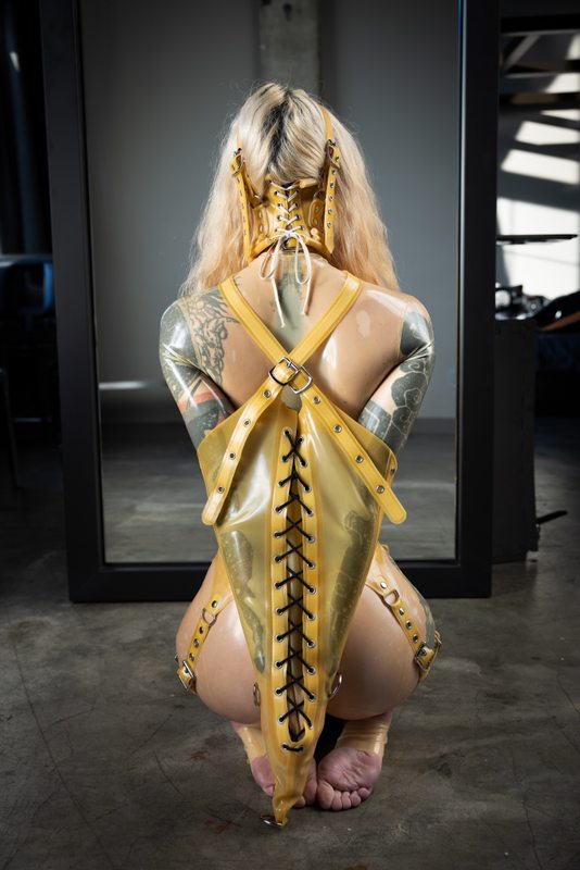 A sexy photograph of Cam Damage, in transparent latex. Tagged with: neck corset & armbinder. Posted April 2021.
