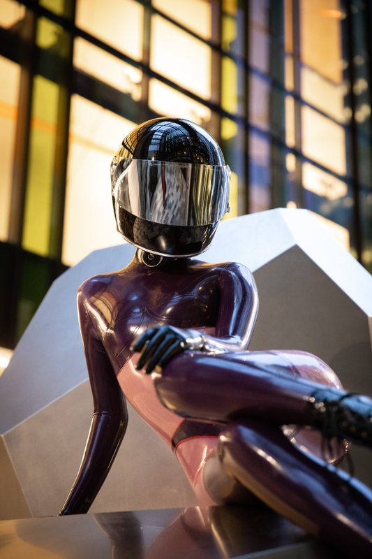 A sexy photograph of Defiantly Yours, in purple & pink & transparent latex. Tagged with: in public & moto helmet. Posted January 2020.