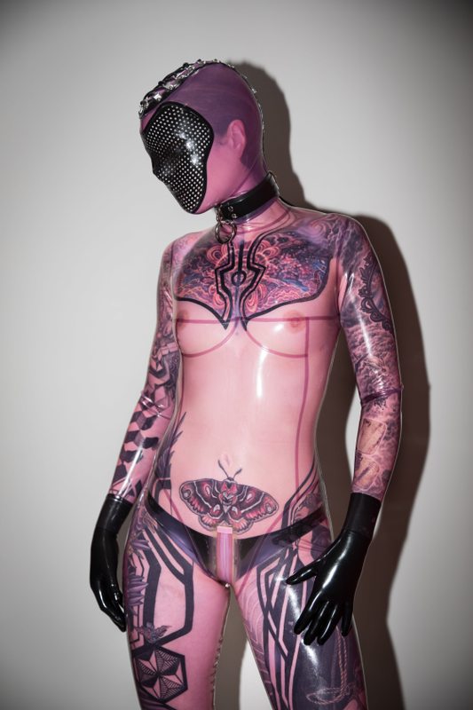 A sexy photograph of Fire Rabbit, in transparent & purple & pink latex. Tagged with: tattoos. Posted December 2017.