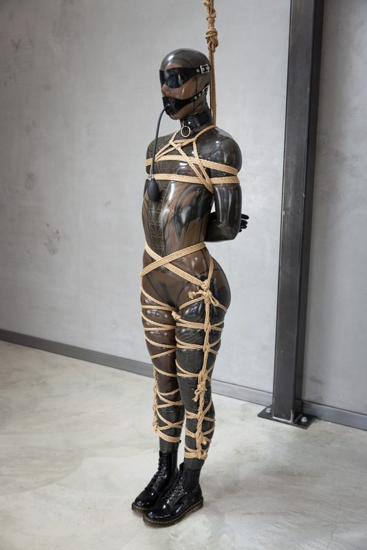 A sexy photograph of Cam Damage in transparent & black latex. Tagged with: rope / shibari & gags. Posted May 2024.